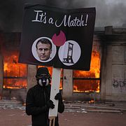 En demonstrant håller upp en bild på president Emmanuel Macron framför en brinnande turistbyrå i Lyon på lördagen.