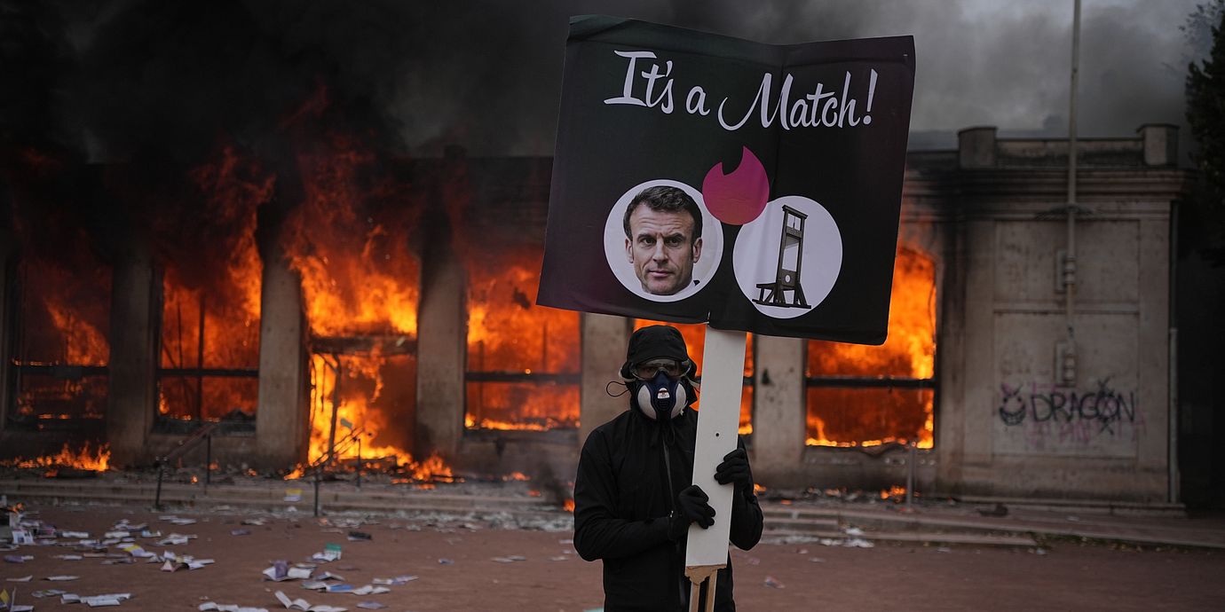 En demonstrant håller upp en bild på president Emmanuel Macron framför en brinnande turistbyrå i Lyon på lördagen.
