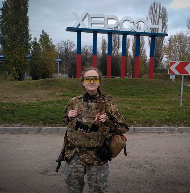 A Ukrainian female soldier poses for a photo against a Kherson sign in the background, in Kherson, Ukraine, Friday, Nov. 11, 2022.  Dagaz / AP