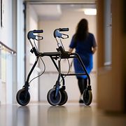 Rullator med ett vårdbiträde i bakgrunden.