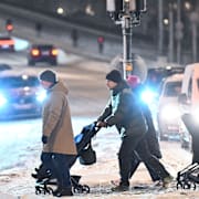 Trafik och fotgängare vid ett övergångsställe på snötäckt gata på Södermalm i Stockholm.