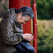 En äldre kvinna sitter på en parkbänk i Peking och användare sin telefon.