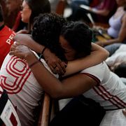 Två kvinnor iklädda Flamengo-kläder kramas under en mässa till minne av offren.