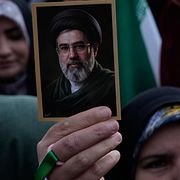 En kvinna håller upp Mojtaba Khameneis porträtt.