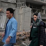 Två personer går förbi en förstörd byggnad i Teheran.