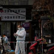 Man i skyddsutrustning framför en avstängd stadsdel i Peking.