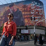 Kvinna promenerar i Teheran, i bakgrunden syns en bild på iranske forne högste ledaren Ali Khamenei.