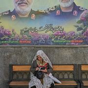 En kvinna sitter under ett porträtt av två tidigare befälhavare inom Irans revolutionsgarde i Teheran.