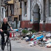 Kvinnan cyklar förbi ett raserat hus i Mariupol.