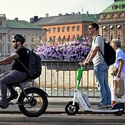 Människor passerar gående, cyklande  och på elsparkcykel på Strömbron med UD i bakgrunden.