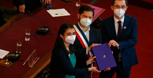 Chiles president Gabriel Boric (i mitten) tar emot det första utkastet till ny konstitution av Maria Elisa Quinteros och Gaspar Dominguez från rådet som utarbetat förslaget. Luis Hidalgo / AP