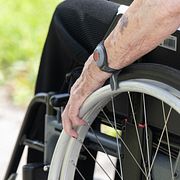 Pensionär med trygghetslarm på armen sitter i en rullstol.