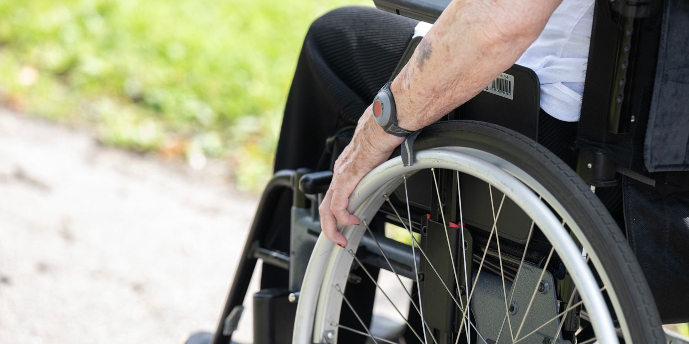 Pensionär med trygghetslarm på armen sitter i en rullstol.