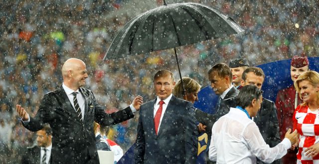 Vladimir Putin med paraply över huvudet. Till vänster Fifapresident Gianni Infantino och till höger Emmanuel Macron och Kolinda Grabar-Kitarovic. KAI PFAFFENBACH / TT NYHETSBYRÅN