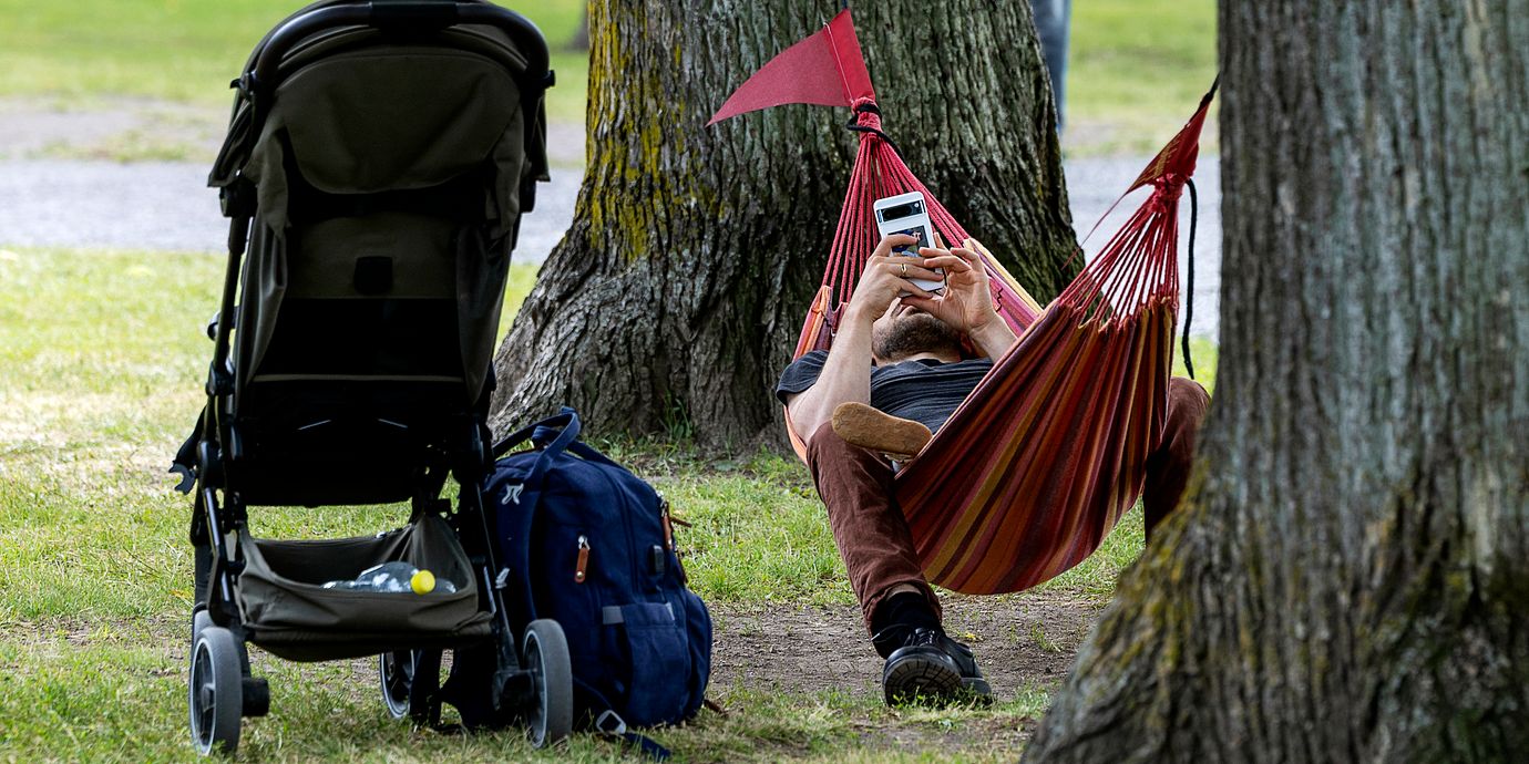 En man vilar i en hängmatta och skrollar på sin telefon.