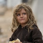 En flicka äter en smörgås utanför ett tält i ett flyktingläger i Gaza, 10 december.