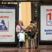 Människor på en busshållplats i St Petersburg, som dekorerats med valaffischer. 