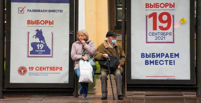 Människor på en busshållplats i St Petersburg, som dekorerats med valaffischer.  Dmitri Lovetsky / TT NYHETSBYRÅN