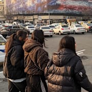 Människor framför en affisch i Teheran som föreställer ett förstört amerikanskt hangarfartyg. 