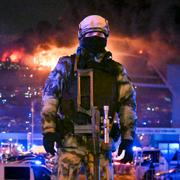 A Russian Rosguardia (National Guard) servicemen secures an area as a massive blaze seen over the Crocus City Hall.