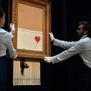 Sotheby’s-anställda håller upp Banksy-verket ”Flicka med ballong”, som till hälften strimlades efter auktionen förra veckan. 