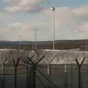 Rahkmat Akilov nya utsikt. Taggtrådsstängsel och skogsklädda berg sedda inifrån Saltvik i Härnösand.