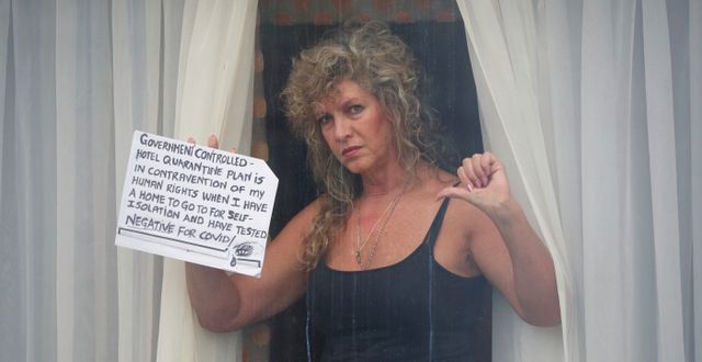 En kvinna protesterar mot krav på karantän på hotell. ”Jag har ett hem att isolera mig i”, skriver hon på en skylt. Jonathan Brady / TT NYHETSBYRÅN