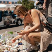 Middle-aged woman with glasses examines vintage porcelain dishes while squatting on flea market.