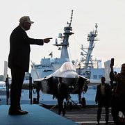 President Donald Trump med hangarfartyget USS Abraham Lincoln i bakgrunden.