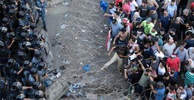 Riot police stand guard as anti-government protesters try to remove a barbed-wire barrier. Beirut, Lebanon, Saturday, Oct. 19, 2019. Hassan Ammar / AP
