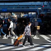 Japansk dam går över en gata i Tokyo med resväska.