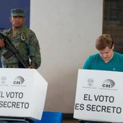 En man röstar i Ecuador medan en säkerhetsvakt vaktar röstlokalen.