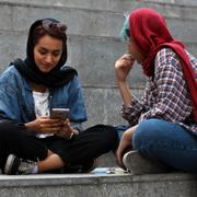 Två unga kvinnor sitter med sina mobiltelefoner i Teheran. 