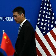 En tjänsteman passerar Kinas och USA:s flaggor inför ett möte i Peking 2023.