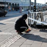 En man lägger blommor vid polisens avspärrningar på Vårväderstorget i Göteborg.