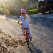 Flicka med cykelhjälm cyklar på gata. Illustrationsbild.