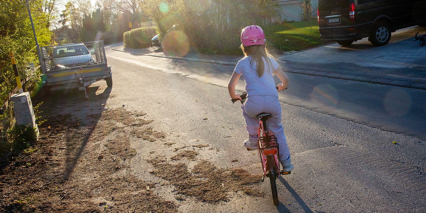Flicka med cykelhjälm cyklar på gata. Illustrationsbild.