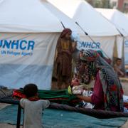 Kvinna med barn i ett flyktingläger i Pakistan med UNHCR:s tält i bakgrunden. 