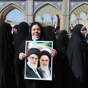 En iransk kvinna med ett porträtt på ayatollorna Khamenei och Khomeini.