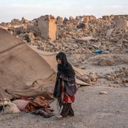 En kvinna framför sitt förstörda hus i Afghanistan.