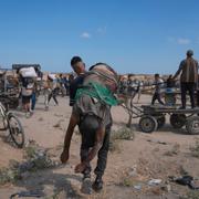 En palestinsk man bär en man som har dödats i närheten av en GHF-distribution i början av augusti.