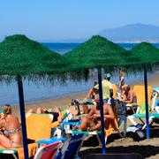 Arkivbild. Turister solar på solstolar under parasoll på en badstrand i Malaga i Spanien. 