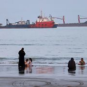 Badbesökare på en strand medan handelsfartyg ligger för ankar i Hormuzsundet utanför Bandar Abbas i Iran den 5 augusti 2026.