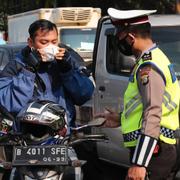 En polisman ber en motorcyklist att ta på sig munskyddet vid en vägkontroll i Jakarta. 