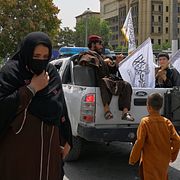En kvinna passerar förbi talibankrigare som firar den fjärde årsdagen av sitt maktövertagande i Kabul, Afghanistan den 15 augusti 2025.