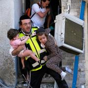 En räddningsarbetare bär två barn efter en iransk attack mot Haifa i Israel på söndagsmorgonen. 