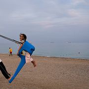 Oljetankers och fraktfartyg ligger på rad i Hormuzsundet utanför Khor Fakkan i Förenade arabemiraten, medan barn leker i förgrunden.