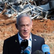 Benjamin Netanyahu framför en byggnad som skadades under kriget med Iran.
