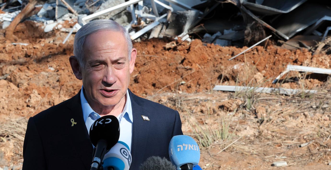 Benjamin Netanyahu framför en byggnad som skadades under kriget med Iran.
