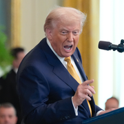 Donald Trump vid en pressträff bredvid Coca-Cola-burkar på en hylla.